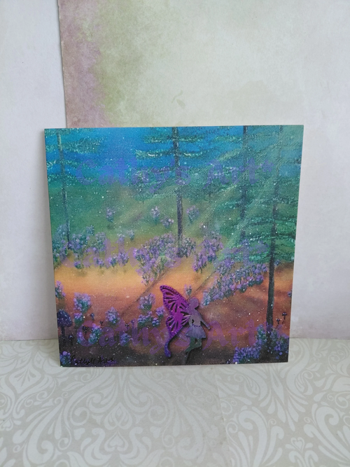 A square printed greeting card featuring a colourful forest scene with tall trees, purple bluebell flowers, and a purple fairy, displayed against a textured light wall. Original artwork printed greeting card by Cathy's Art*