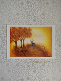 A art print featuring a painted autumn landscape with three trees, a stag, and a glowing yellow-orange sky, displayed against a patterned grey wallpaper background. The print has a white border. Artwork is by Cathy's Art* 