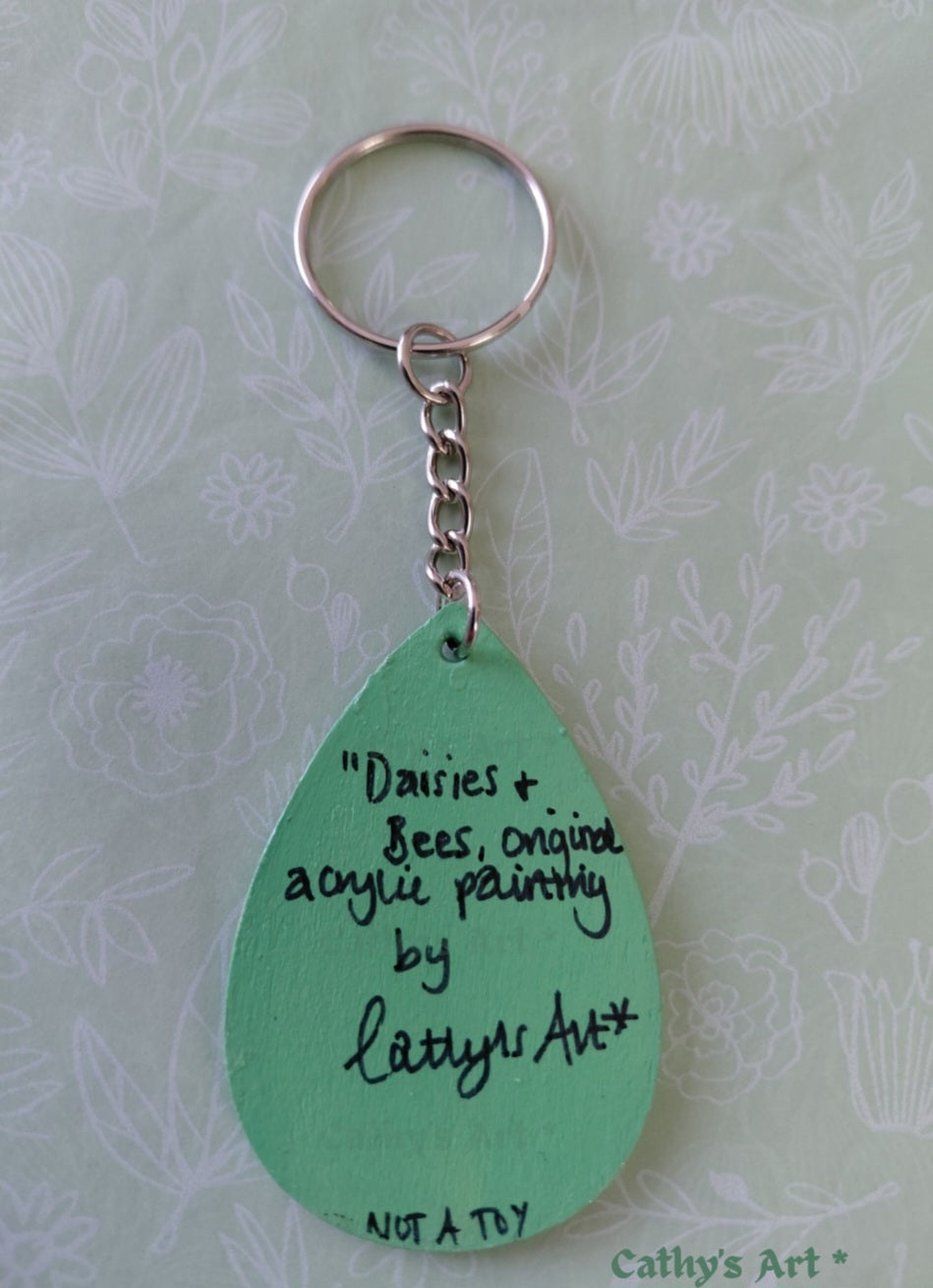 A mint green teardrop-shaped keychain with a silver metal split ring and chain, featuring a handwritten quote on a light patterned background. Daises & Bees original acrylic painting by Cathy's art*