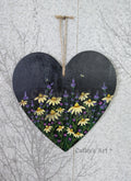 Heart-shaped wooden heart wall plaque with an original painting of yellow daisies, purple lavender, green stems, and small bees, on a black background, suspended by a jute string. Photographed against a light grey textured background. Original acrylic painting by Cathy's Art*
