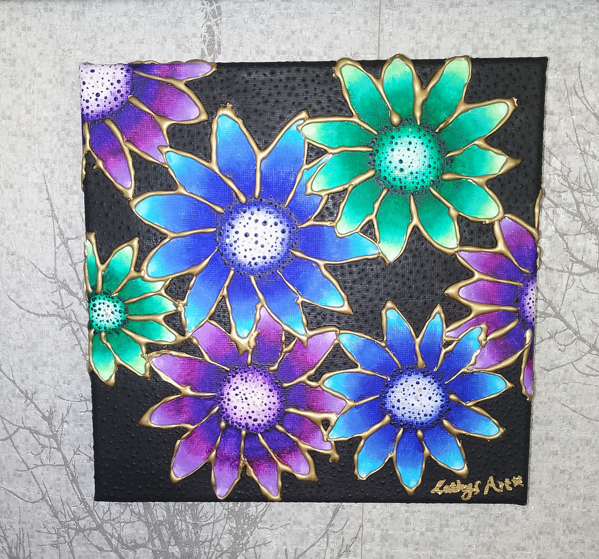 A square black canvas painting featuring vibrant, overlapping daisy-like flowers in shades of blue, purple, and greens, outlined with gold paint. The artwork is displayed against a textured light grey background. Original acrylic sculpture canvas by Cathy's art*