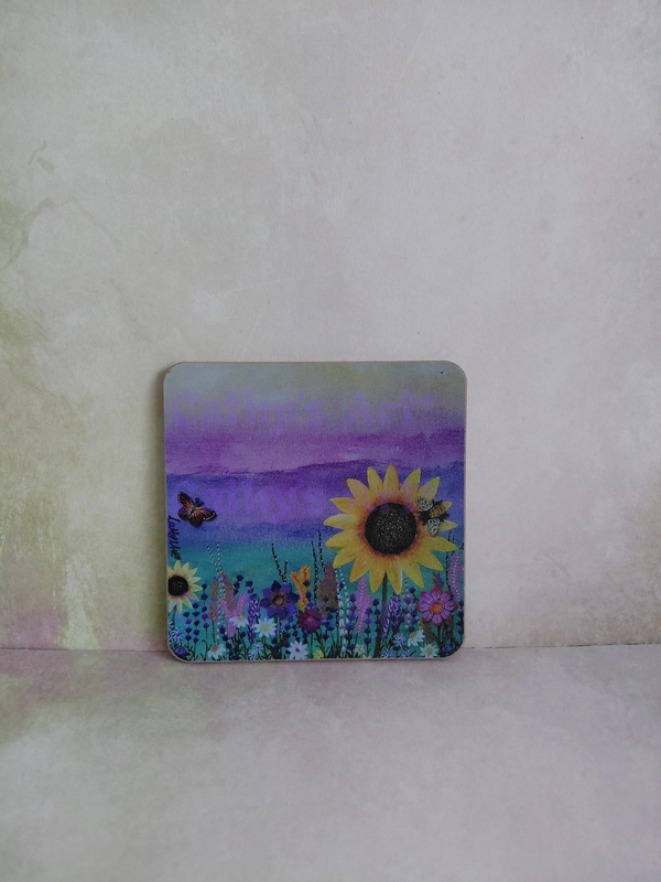A square decorative coaster with rounded corners featuring a colourful painted landscape of sunflowers, wildflowers, a butterfly, a bee and a purple sky, displayed on a textured light beige surface. Original artwork printed coaster by Cathy's Art*