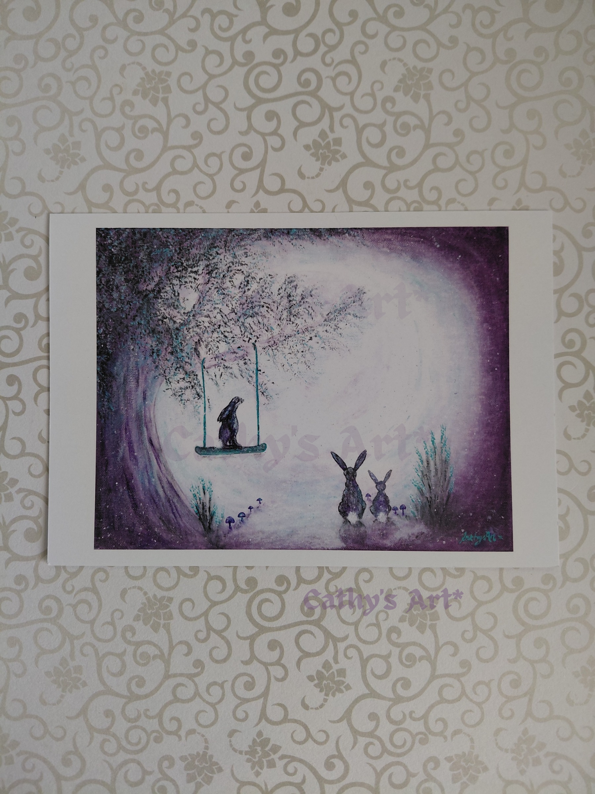 A whimsical scene featuring a tree, glowing moon, three hares starring at the moon, one sat on a swing in the tree. Purple and turquoise colours. Artwork by Cathy's Art*