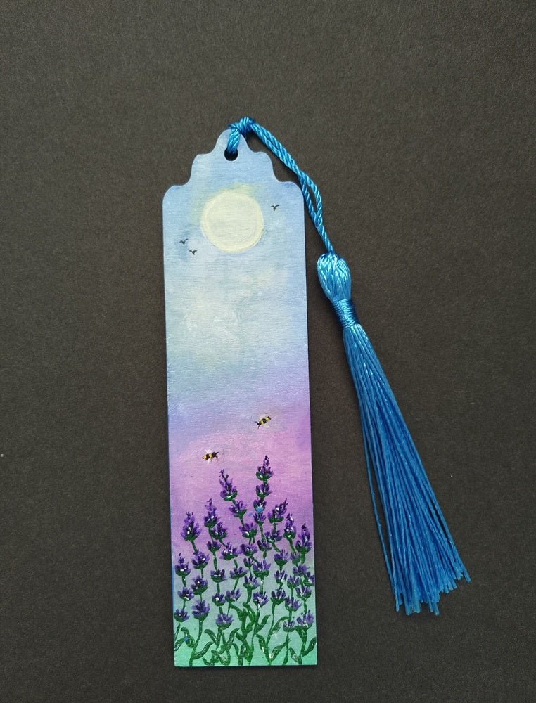 A hand painted bookmark with a blue tassel, featuring a painted lavender field under a yellow and purple sky on a black background. By Cathy's Art*