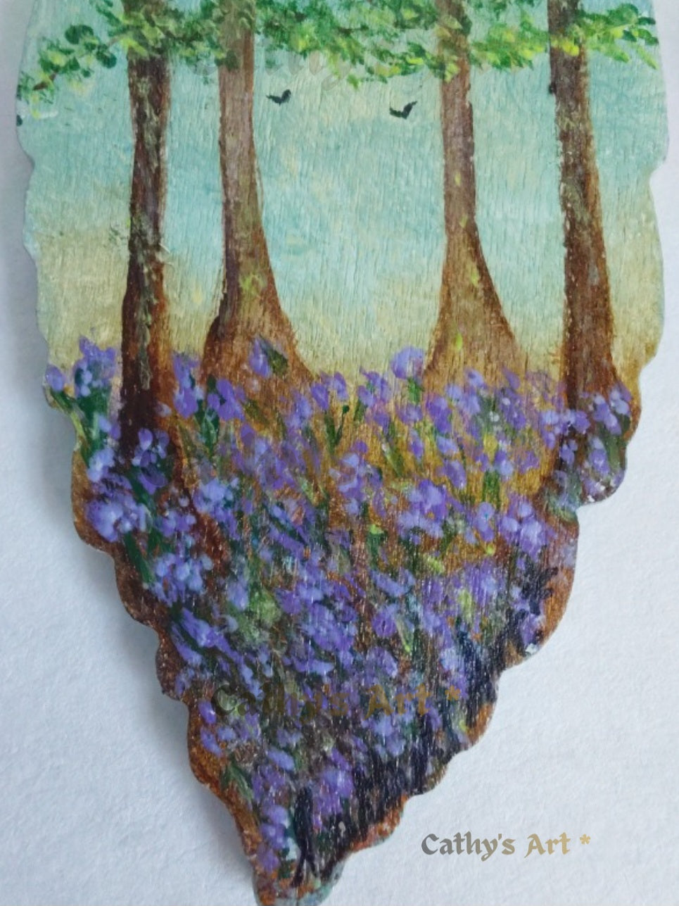 A close up of hand painted forest scene with green trees and purple bluebell flowers below the trees, displayed on a light background. Original hand painted bookmark by Cathy's Art*