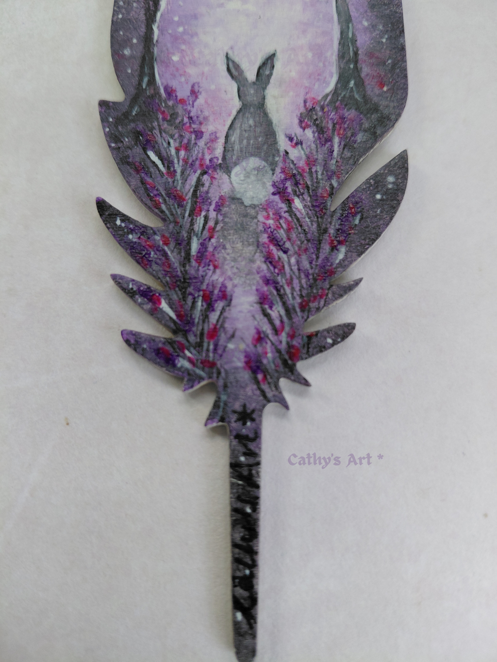 Bottom half of a hand painted feather showing a hand painted scene of a hare sat on a path with lowers either side. In purple, white and grey colours. Original hand painted acrylic painting on a feather bookmark. by Cathy's Art*