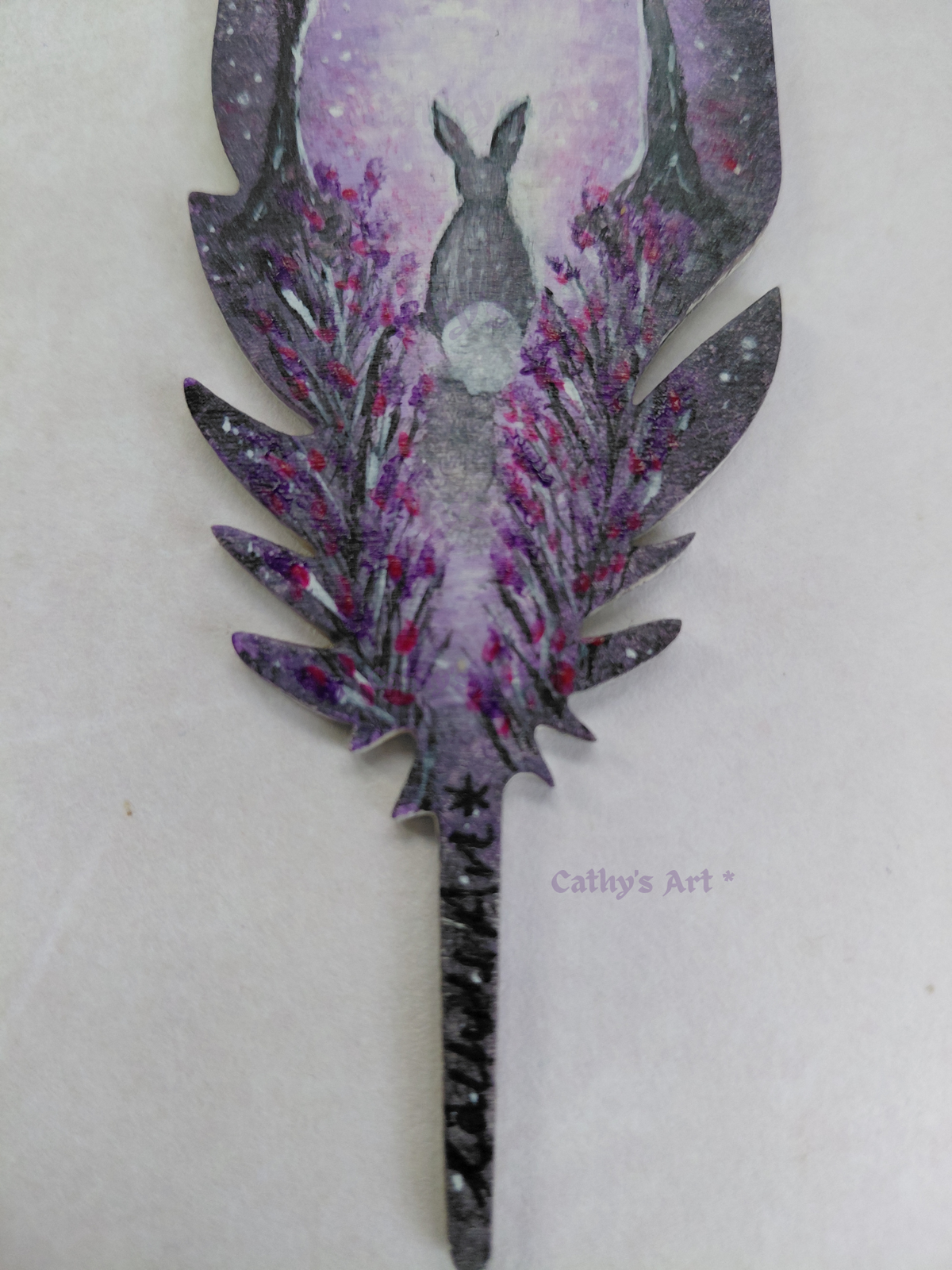 Bottom half of a hand painted feather showing a hand painted scene of a hare sat on a path with lowers either side. In purple, white and grey colours. Original hand painted acrylic painting on a feather bookmark. by Cathy's Art*