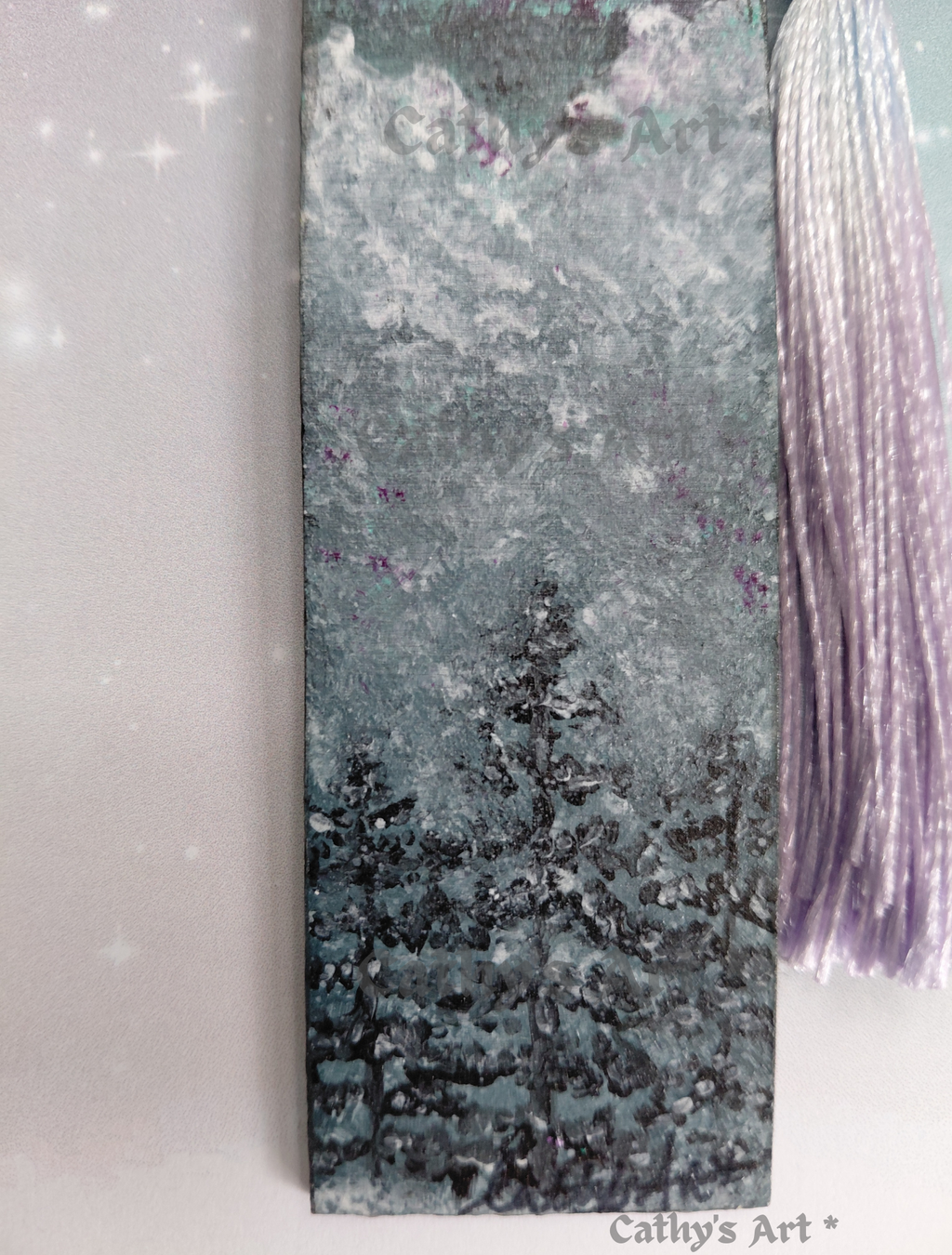 Bottom park of a hand painted bookmark, featuring snow capped fir trees and mountains, with a lilac tassel. Original acrylic hand painted bookmark by Cathy's Art*