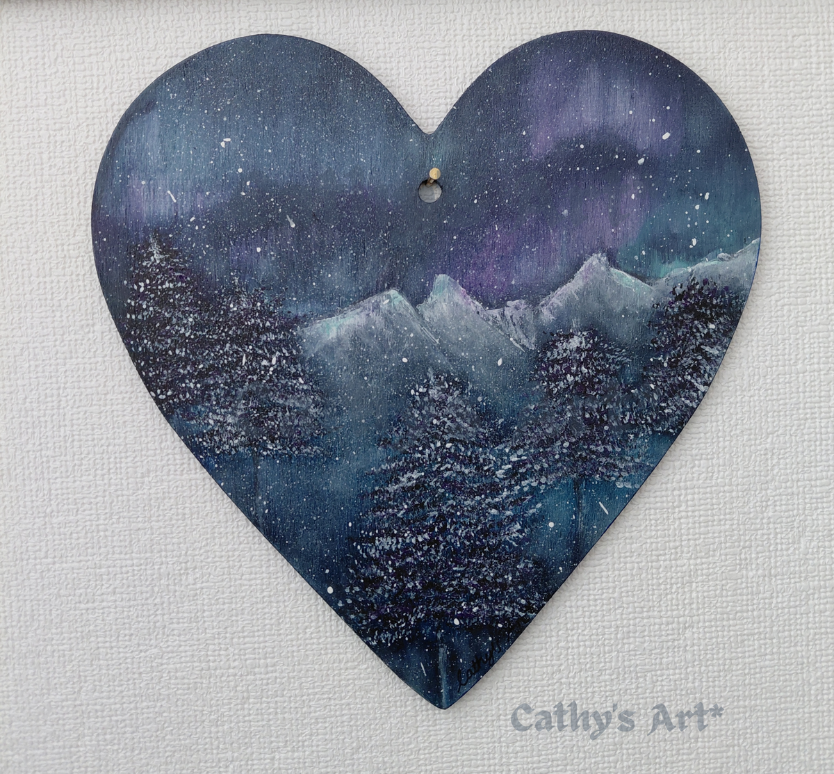 A winter scene on a heart shape, with dark fir trees, snow capped mountains, featuring the Aurora Borealis in the sky in colours of purples and turquoise blues on a dark grey background. On plain white background. Original acrylic painting on wooden heart by Cathy's Art*