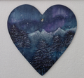 A winter scene on a heart shape, with dark fir trees, snow capped mountains, featuring the Aurora Borealis in the sky in colours of purples and turquoise blues on a dark grey background. Original acrylic painting on wooden heart by Cathy's Art*