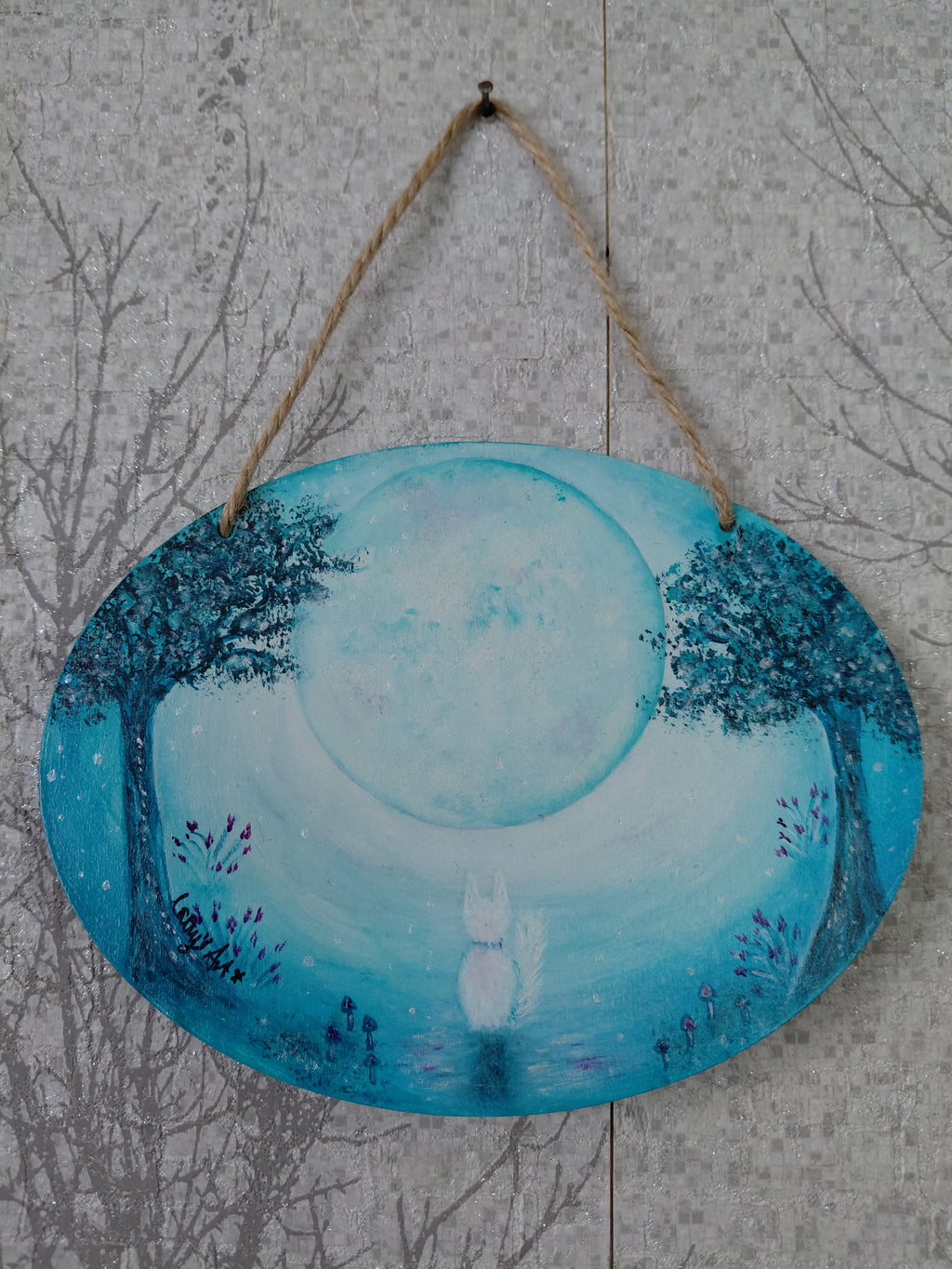 An oval hanging wall plaque featuring a hand painted magical scene with a large pale moon, blue trees, and a small white cat at the bottom, where violet flowers and tiny mushrooms grow, suspended by a natural jute rope against a grey textured background. Original acrylic painting on wooden oval plaque by Cathy's Art*