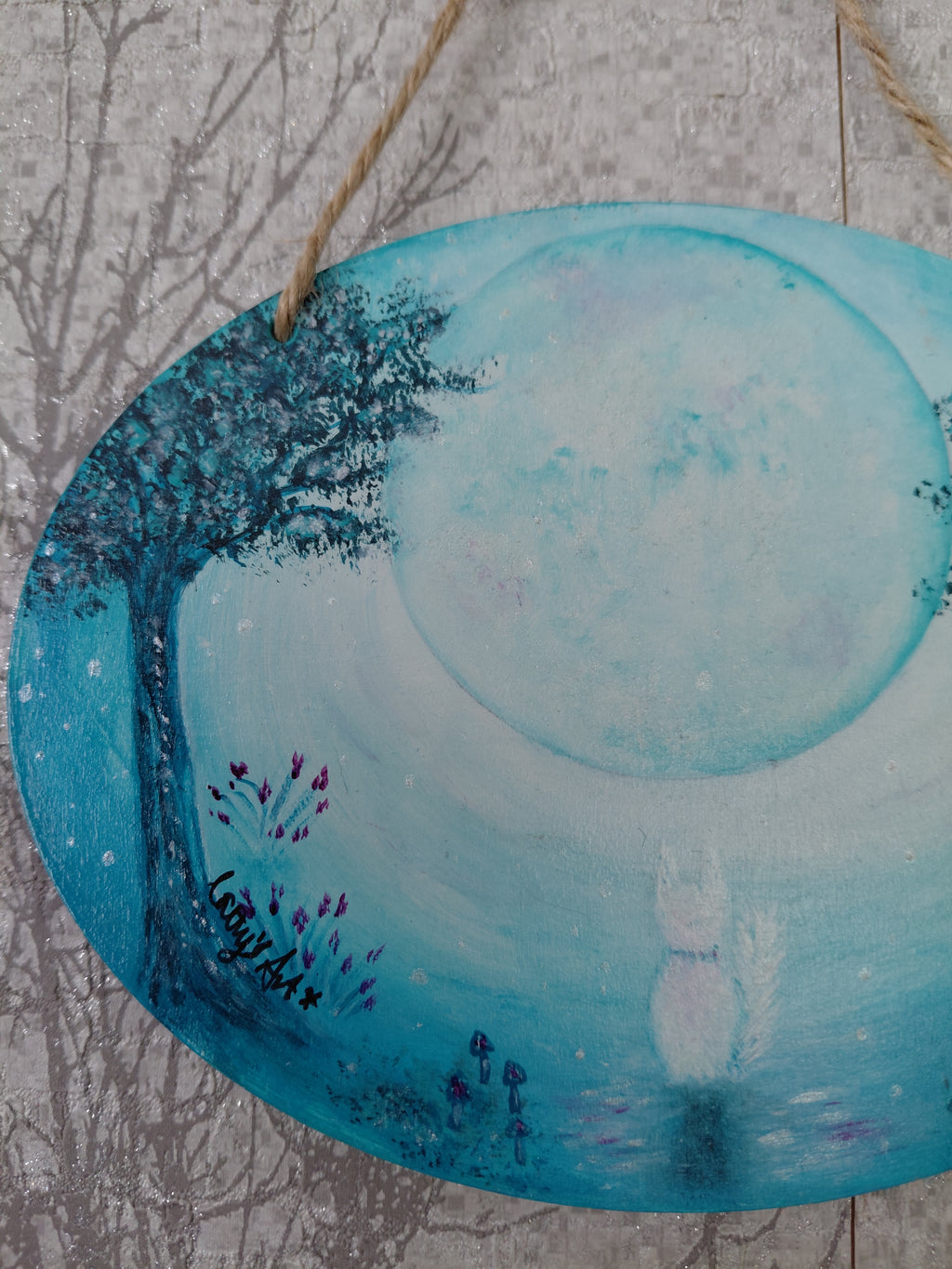 An oval wooden hanging plaque featuring a hand painted whimsical moon night scene with a large glowing full moon, a dark tree on the left, and a white cat silhouette near the bottom centre. The plaque hangs from a jute string against a textured grey background. Original acrylic painting by Cathy's Art*