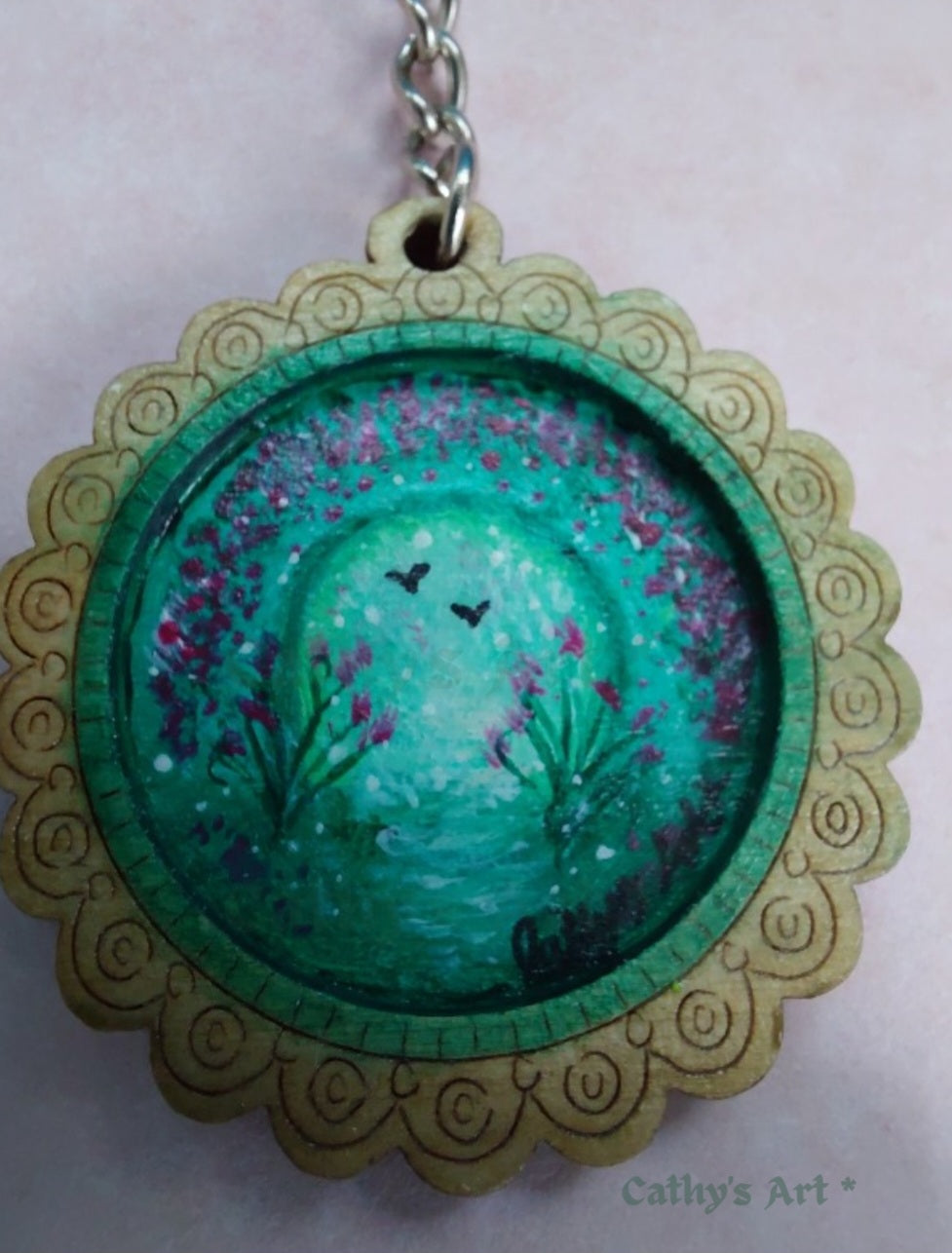 A circular wooden keyring featuring a hand-painted fantasy scene of a green land with violet flowers and two black birds, surrounded by a scalloped frame. Original painted keyring by Cathy's Art*