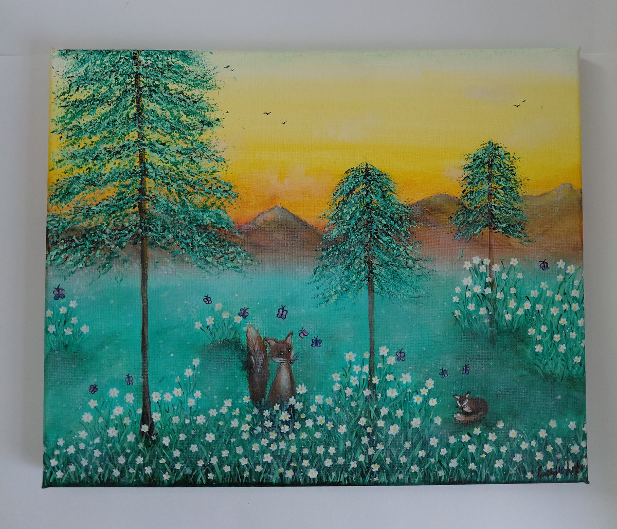 A painted forest scene at sunset with tall green trees, a yellow-orange sky, distant mountains, and a field of white flowers. Two foxes are visible in the meadow, one standing and one lying down. On a plain white background. An original canvas painting by Cathy's Art*