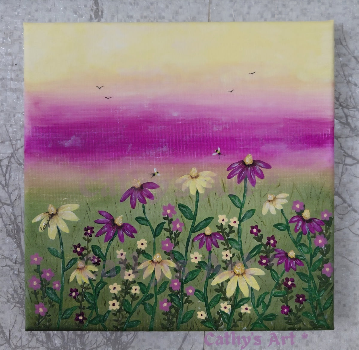 A square canvas painting of a wildflower  meadow, featuring purple and yellow daises on green stems against a pastel sky with pink, purple, and yellow gradients. Birds fly in the distance and bees dance above the flowers. The canvas is displayed on a textured grey background. Original acrylic canvas painting by Cathy's Art*