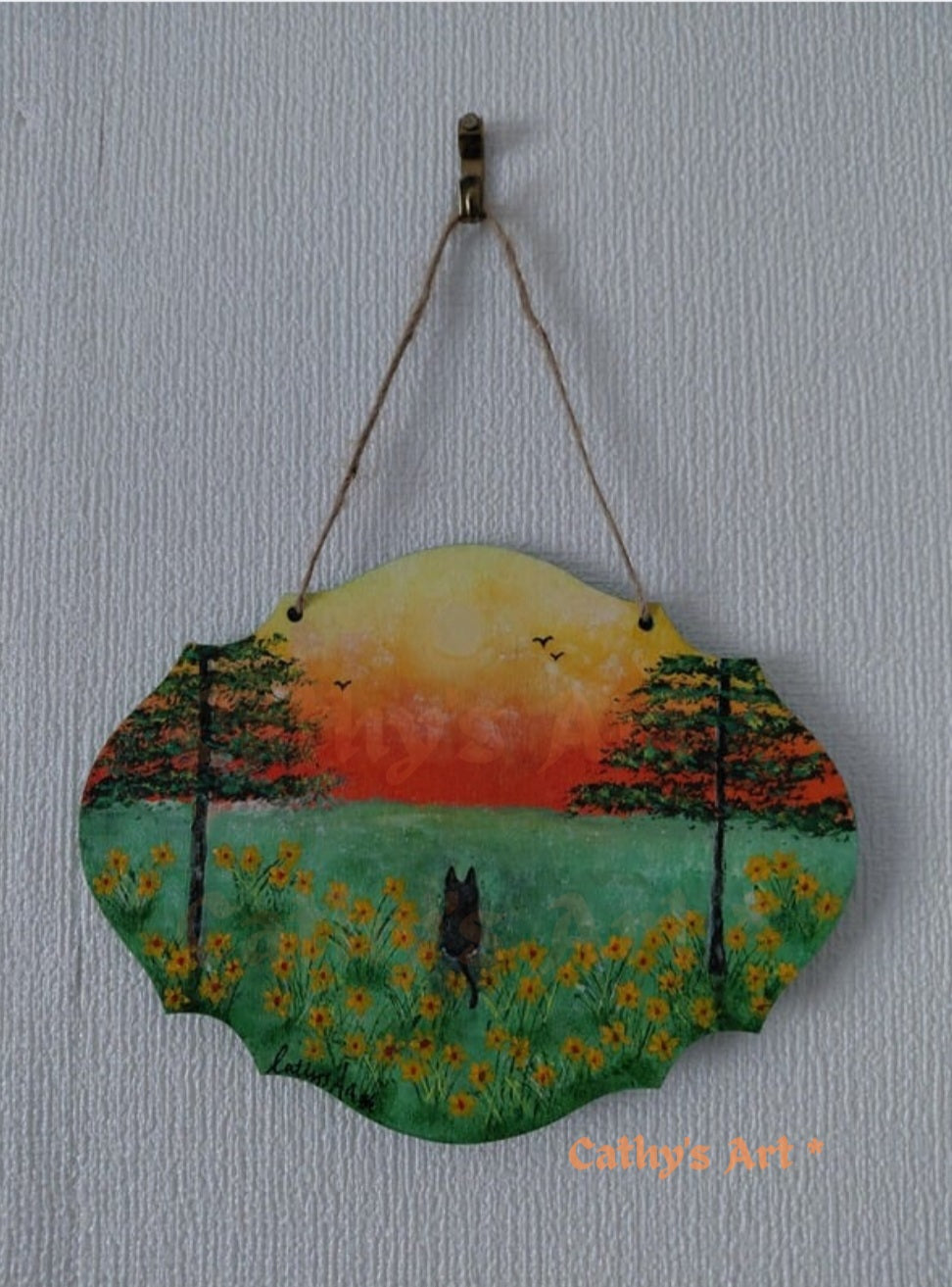 A scalloped wooden hanging plaque featuring a hand-painted landscape of a black cat in a field of yellow flowers at sunset, featuring two trees and birds flying in the sky. Hung on a white textured wall with jute string. Original acrylic painting on a wooden plaque by Cathy's Art*