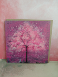 A square printed greeting card featuring a pink cherry blossom tree, displayed leaning against a textured pink wall on a light-coloured floor. With a kraft envelope behind. Original artwork printed greeting card by Cathy's Art*