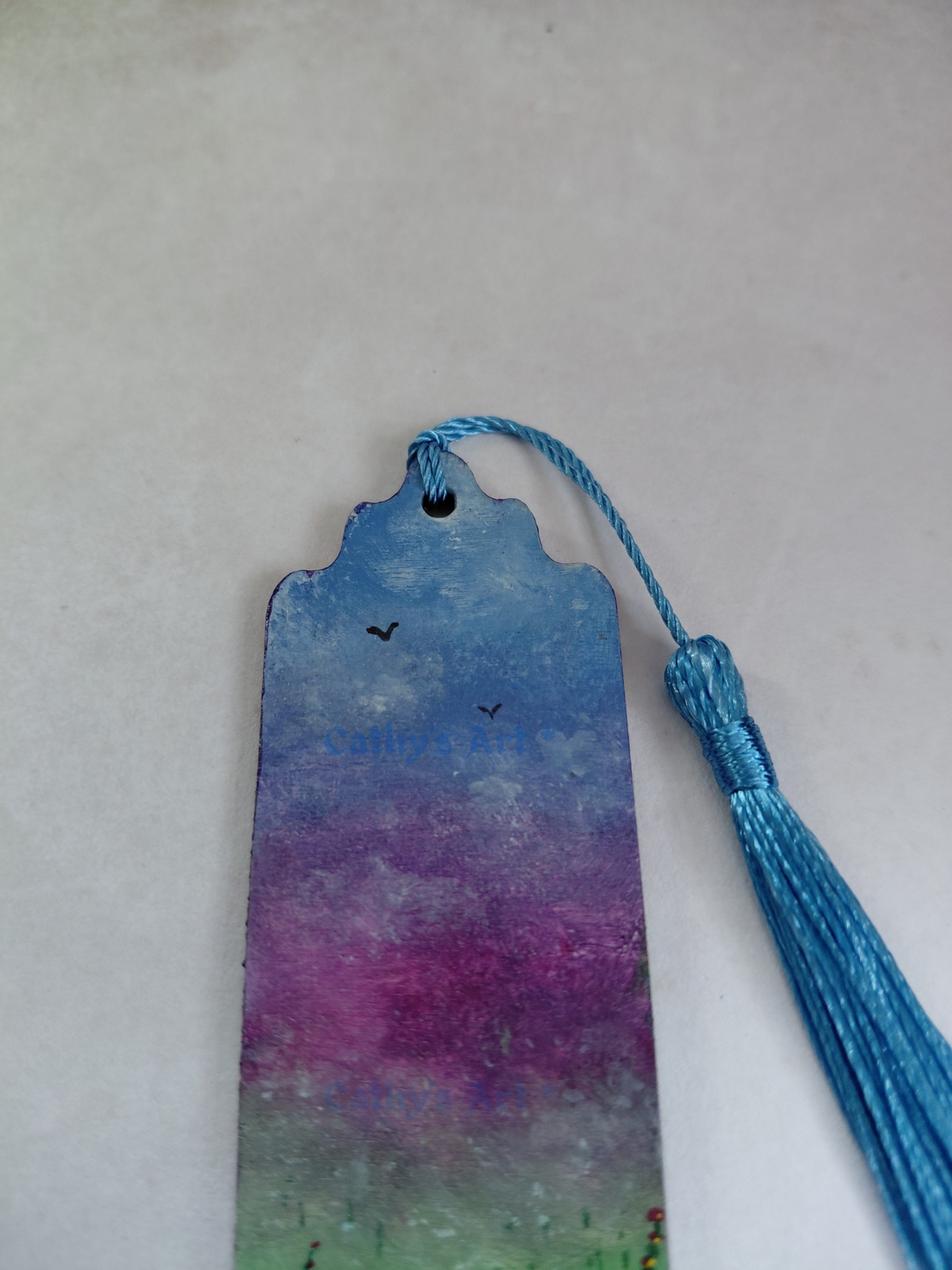 A hand painted wooden bookmark with a blue tassel, featuring a blue and violet sky with small bird silhouettes. Showing the top half of the bookmark. Original hand painted bookmark by Cathy's Art*