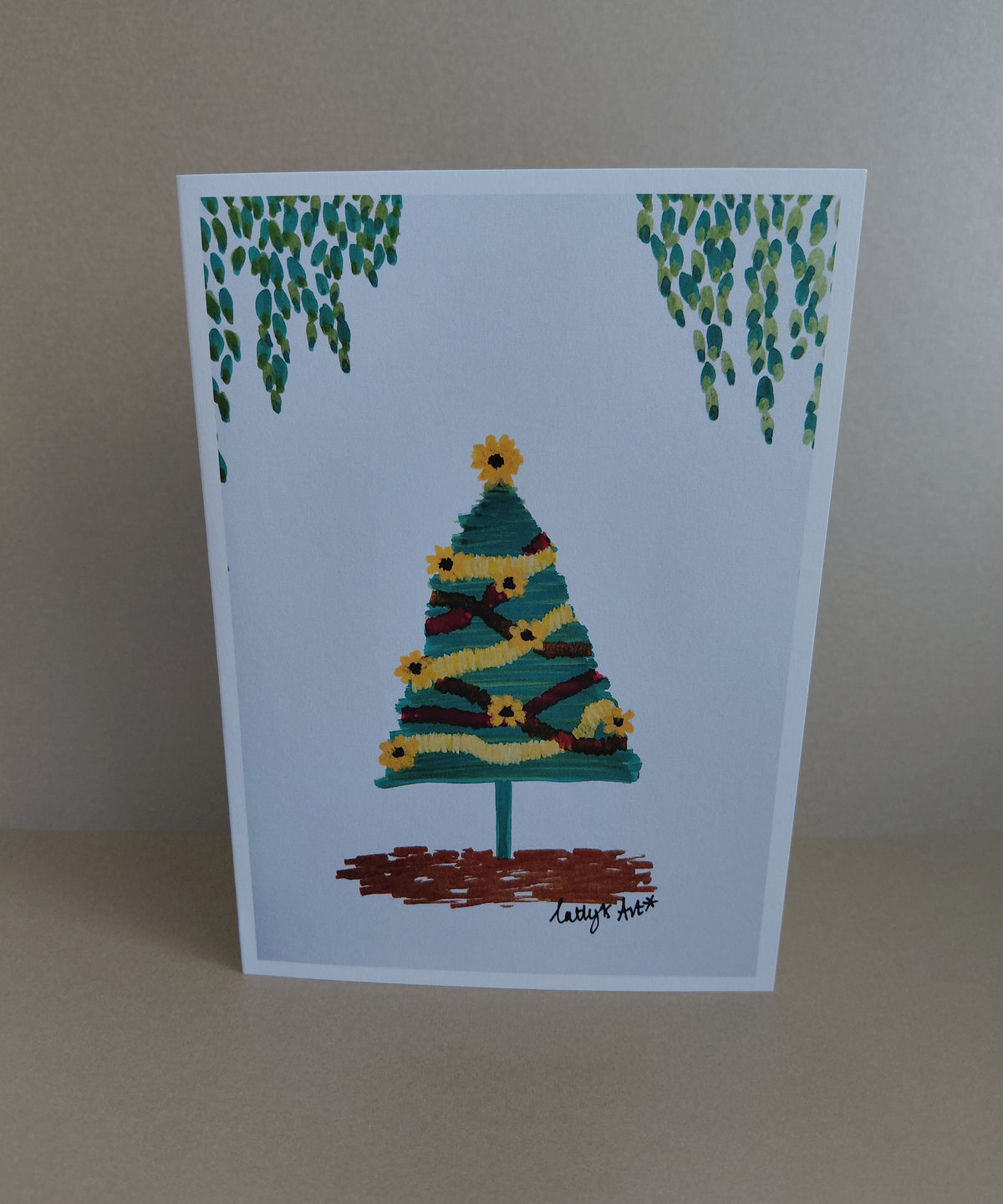 A printed artwork Christmas Card with a sunflower Christmas tree with sunflowers and tinsel. Leavy foliage hangs above the tree. Original artwork & printed by Cathy's Art*