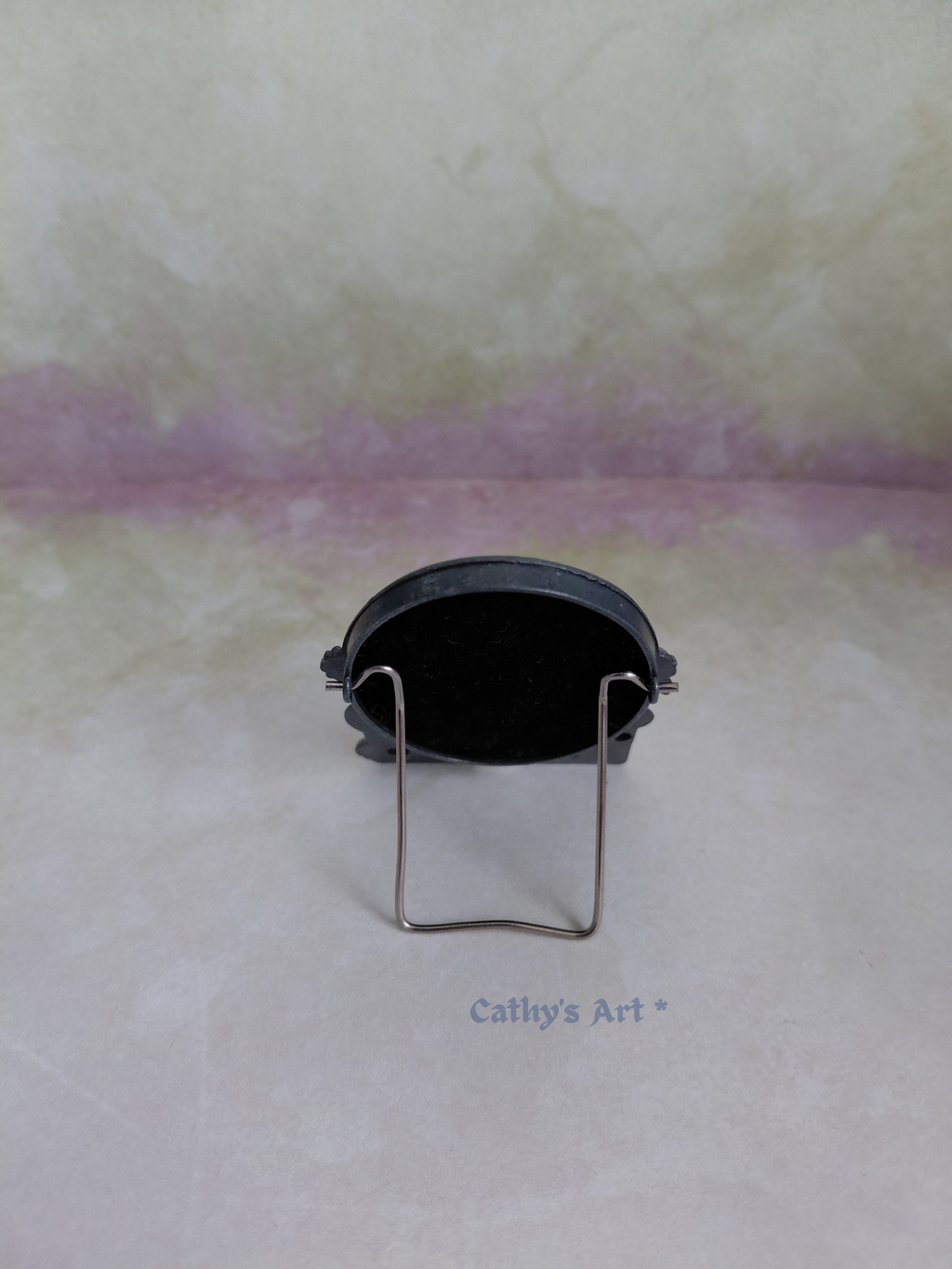 The back of a miniature metal picture frame with a silver metal stand. On a lilac textured background. 