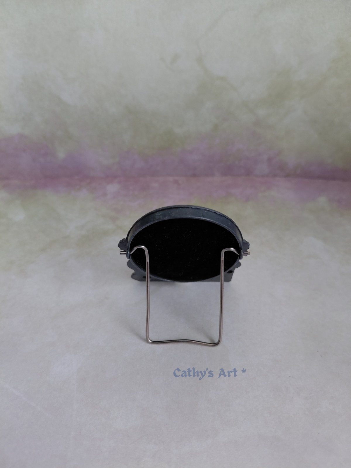 The back of a miniature metal picture frame with a silver metal stand. On a lilac textured background. 