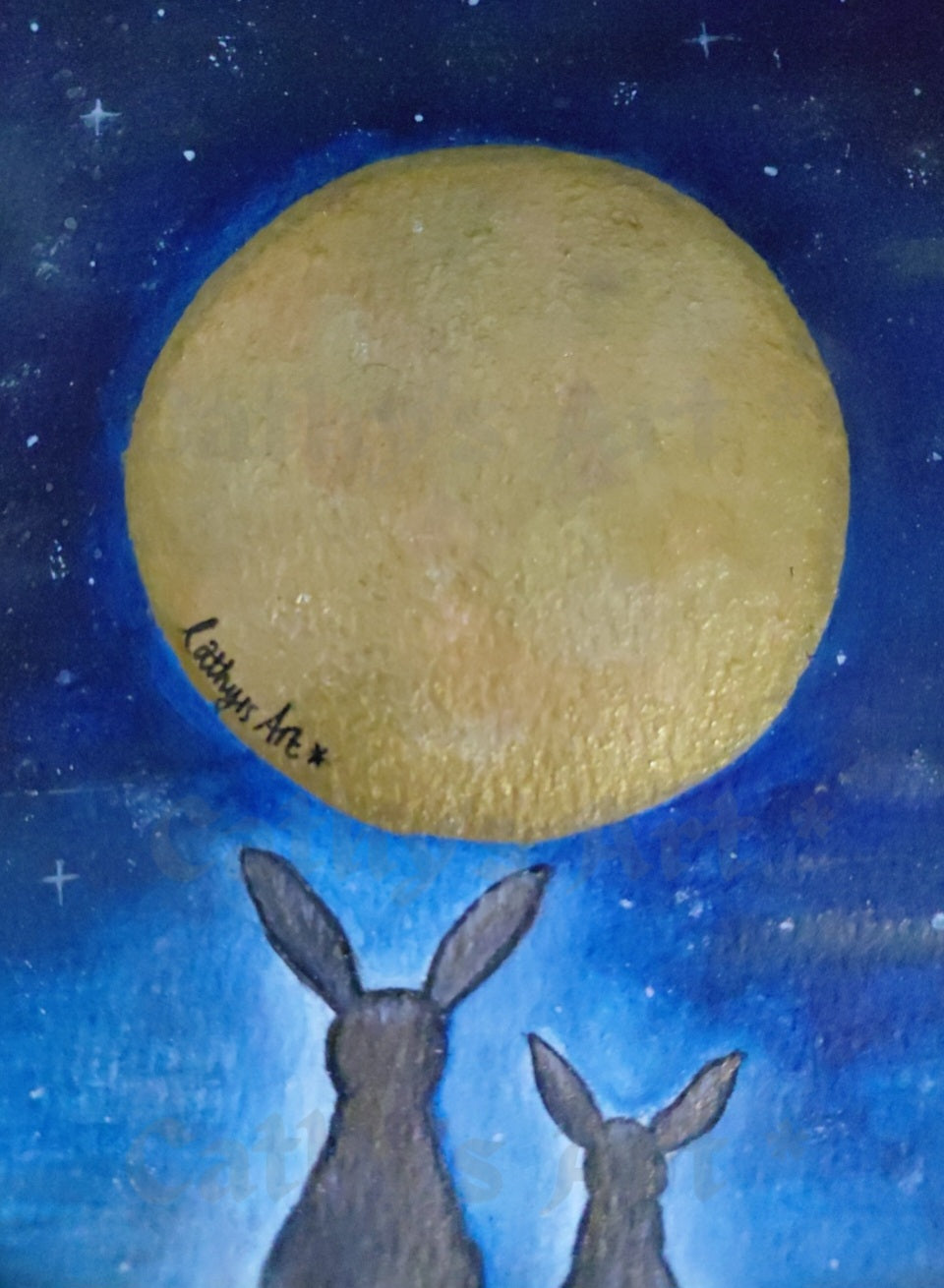A painting of two dark hare silhouettes looking up at a large golden-yellow full moon against a deep blue starry night sky. The artist's signature 'Cathy's Art*' is visible on the left side of the moon. original acrylic painting by Cathy's Art*