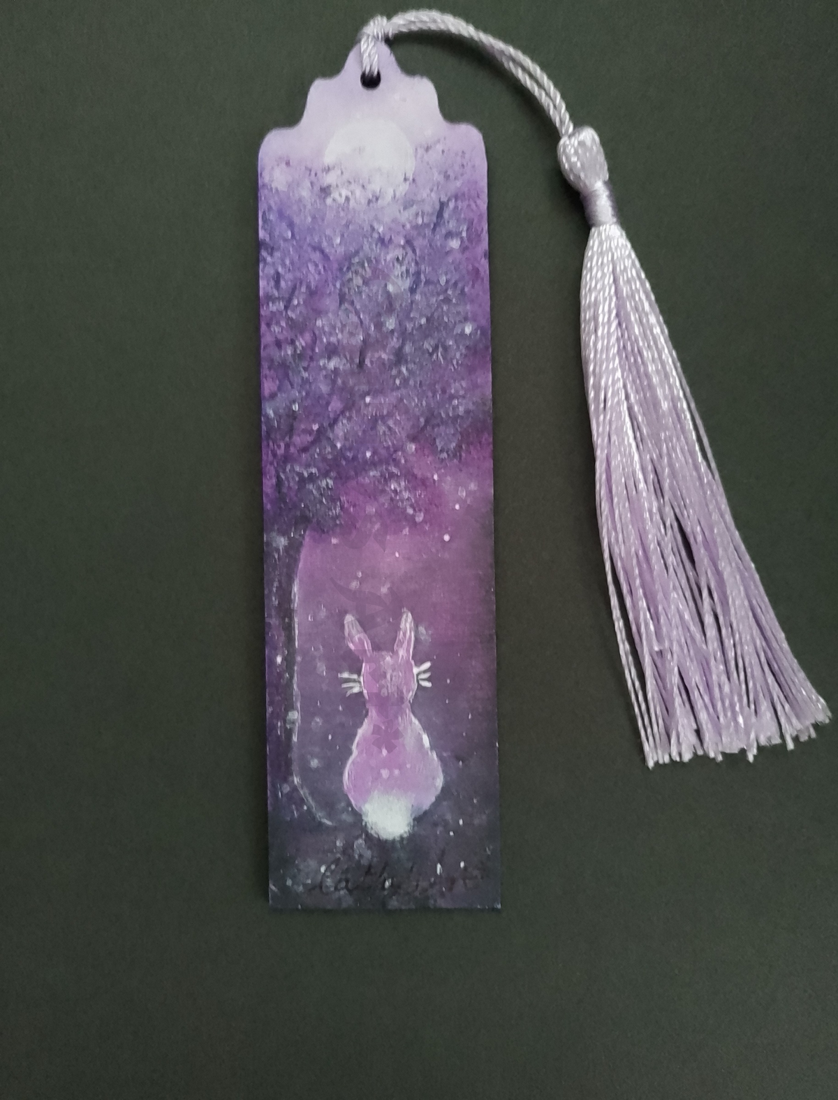 A hand painted wooden bookmark with a tassel, featuring a purple forest illustration with a hare and moon, shown against a black background. By Cathy's Art*