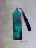 A hand painted whimsical bookmark in turquoise, purple, black and green colours. A black cat sits under a tree, birds fly in the sky, purple flowers bloom, magical orbs dance in the air. With purple tassel, on a textured pale lilac and green . Original hand painted bookmark by Cathy's Art*