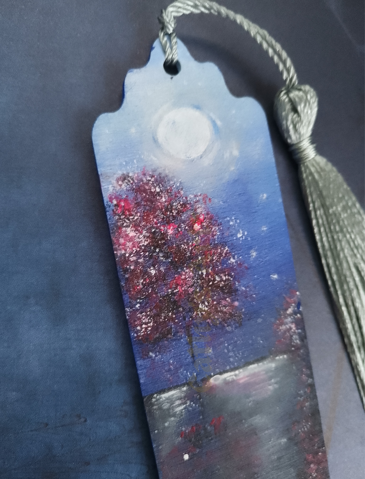 A close up image of a hand painted bookmark with a red tree, full moon on a dark night, with silver tassel, on a dark blue background. Original hand painted bookmark by Cathy's Art*